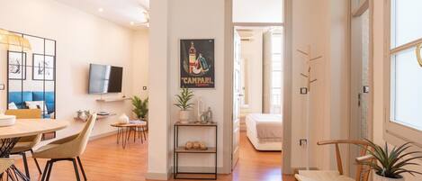 Un espacio de sala moderno con comedor, un televisor montado en la pared y un pasillo que conduce a otra habitación.