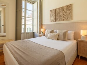 Habitación de hotel con una cama grande, una ventana con vistas, un panel decorativo en la pared y una mesita de noche con una lámpara.