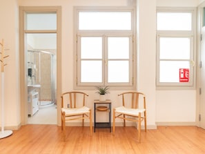 A room with two wooden chairs, a small table with a plant, and a window with an extinguisher sign. - Bright apartment in the heart of Malaga, ideal for long stays (Málaga)