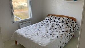 Ein Schlafzimmer mit Bett, Fenster, Heizkörper und einem Regal mit Dekorationen.