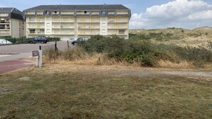 Ein mehrgeschossiges Gebäude mit Balkonen, einem Parkplatz und einer Rasenfläche mit Büschen.