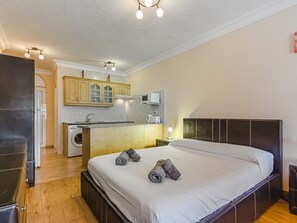 Ein Schlafzimmer mit einem großen Bett, Holzboden, einer Küchenzeile mit Schränken und einer Mikrowelle sowie einer Deckenleuchte.
