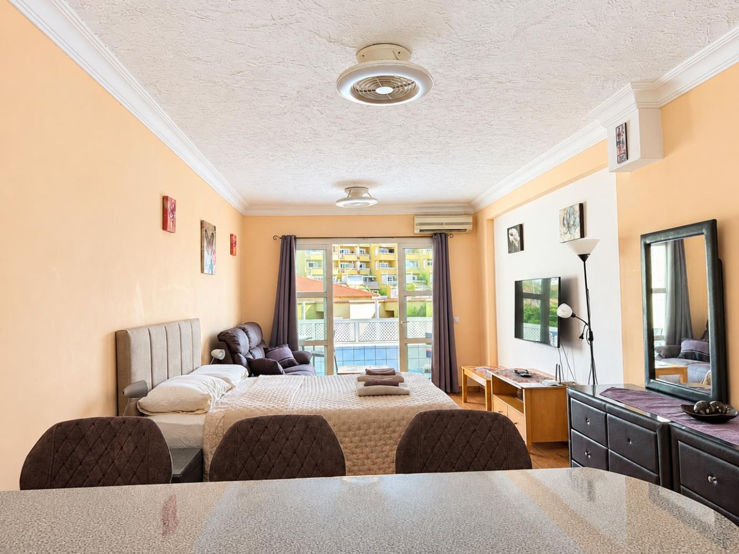 A hotel room with a bed, a desk, a chair, a mirror, and a view of the outside.