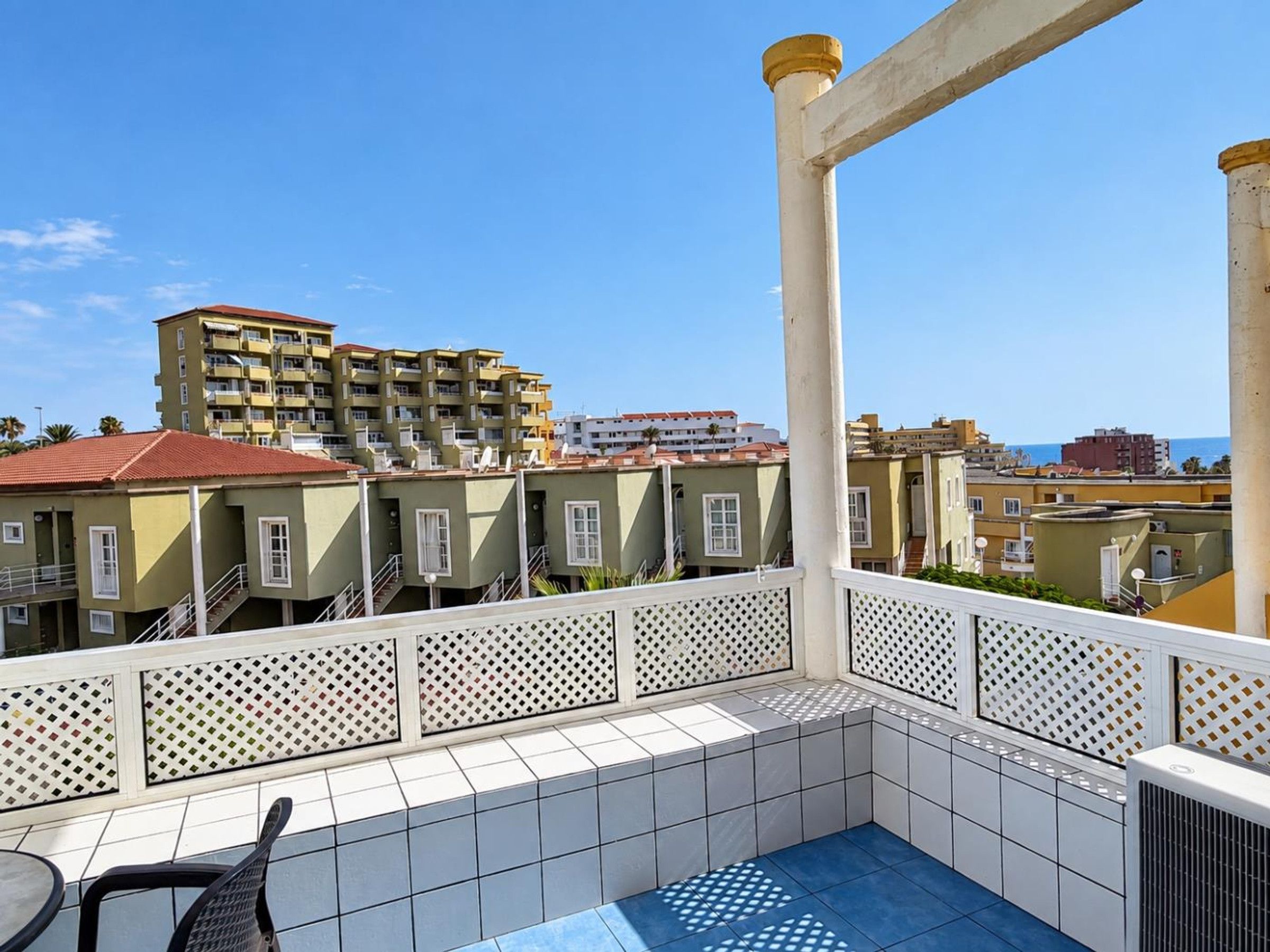 A balcony with a tiled floor, white railings, and a view of surrounding buildings.