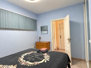 Ein Schlafzimmer mit einem Bett, einer Holzkommode, einer Tür und einem Fenster mit Jalousien.