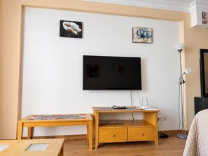 A living room with a flat-screen TV mounted on the wall, a wooden coffee table, a small wooden cabinet, and a floor lamp. - Beautiful 1-bedroom apartment in Costa Adeje, near beach (Costa Adeje)