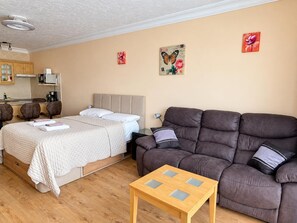 Ein Hotelzimmer mit einem Bett, einer Couch, einem kleinen Tisch und einer Küchenzeile im Hintergrund.