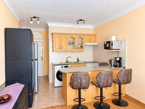 A compact kitchen with a central island, bar stools, a washing machine, and a microwave. - Beautiful 1-bedroom apartment in Costa Adeje, near beach (Costa Adeje)