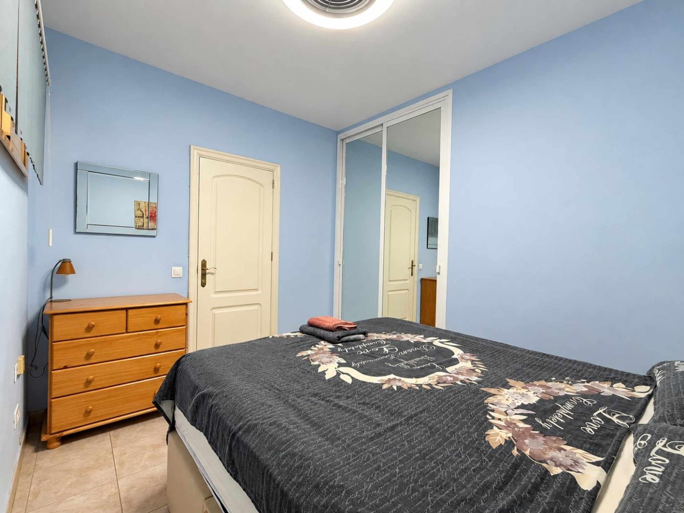 Une chambre à coucher avec un lit, une commode, un miroir et une porte.
