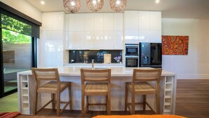 Une cuisine moderne avec des meubles blancs, un îlot central doté de tabourets, une grande fenêtre et un réfrigérateur.