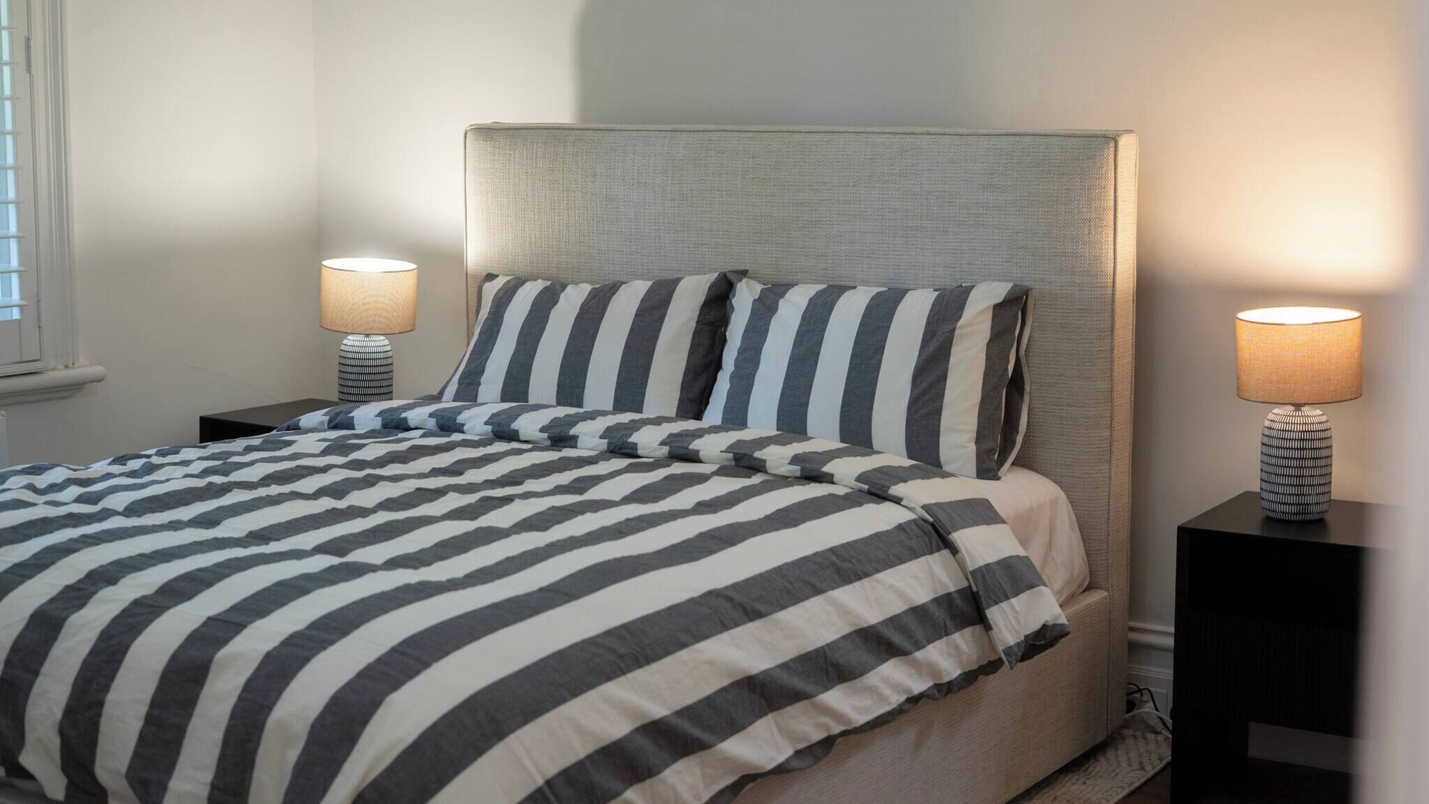 Una cama bien hecha con ropa de cama a rayas, dos mesitas de noche con lámparas y un cabecero.