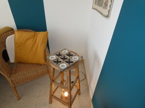 A corner of a room with a wicker chair, a small wooden stool with a board game, and a blue and white wall. - Bohemian Apartment Near Beach - Pets Welcome - Private Parking (Notre-Dame-de-Monts)