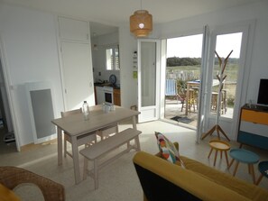A modern living room with a dining area, a sofa, and a TV stand. - Bohemian Apartment Near Beach - Pets Welcome - Private Parking (Notre-Dame-de-Monts)