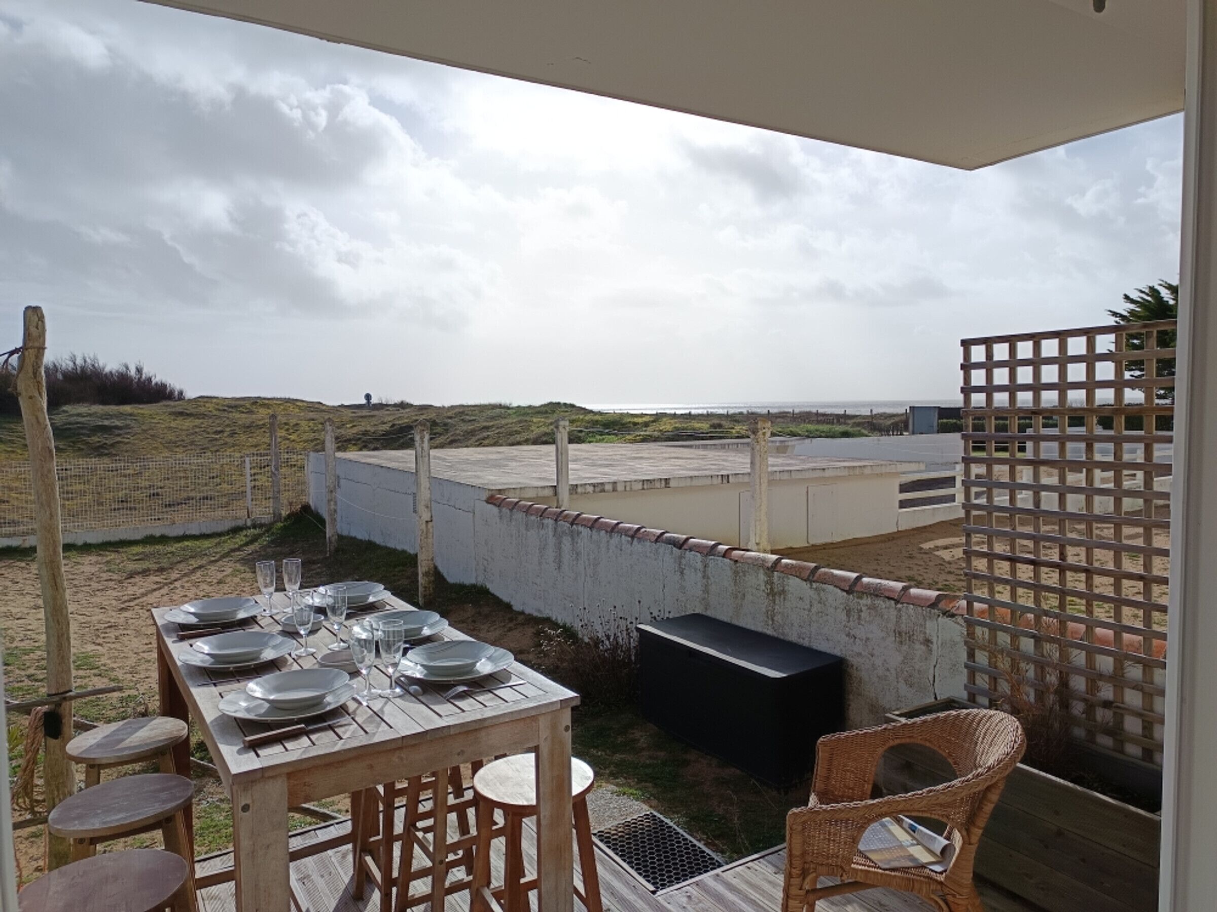 Un comedor al aire libre con una mesa preparada para cuatro, una parrilla y vista a la playa.
