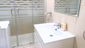 Ein Badezimmer mit Duschkabine aus Glas, einem weißen Waschbecken mit Seifenspender und einem Spiegel darüber.