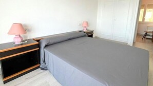 A bedroom with a bed, two bedside tables with lamps, a wardrobe, and a chair in the corner. - Beautiful apartment in Roses with terrace and garage, 600m from the beach (Roses)
