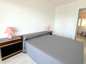 A bedroom with a bed, two bedside tables with lamps, a wardrobe, and a chair in the corner. - Beautiful apartment in Roses with terrace and garage, 600m from the beach (Roses)