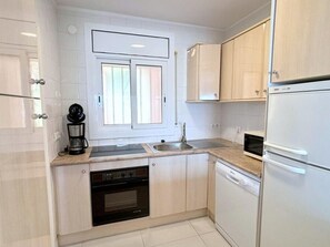 A modern kitchen with white cabinets, a built-in oven, a dishwasher, and a coffee maker. - Beautiful apartment in Roses with terrace and garage, 600m from the beach (Roses)