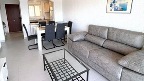 A modern living room with a grey sofa, a glass coffee table, and a dining area with a white table and chairs. - Beautiful apartment in Roses with terrace and garage, 600m from the beach (Roses)