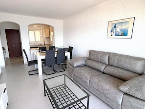 A modern living room with a grey sofa, a glass coffee table, and a dining area with a white table and chairs. - Beautiful apartment in Roses with terrace and garage, 600m from the beach (Roses)