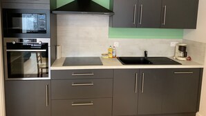 A modern kitchen with a built-in oven, microwave, and stove, a black range hood, and a sink with a coffee maker. - Charming 3-Room Apartment with South Terrace (Chamrousse)