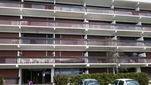 A multi-story building with balconies, a parking area, and a clear sky. - Charming 3-Room Apartment with South Terrace (Chamrousse)