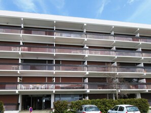 Ein mehrstöckiges Gebäude mit Balkonen, einem Parkplatz und einem wolkenlosen Himmel.