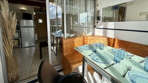 Comedor con mesa lista para cuatro, refrigerador y puerta corrediza de vidrio que da a un balcón.