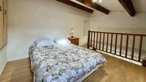 Un dormitorio con cama, vigas de madera en el techo, una mesita de noche y una pequeña mesa con lámpara.