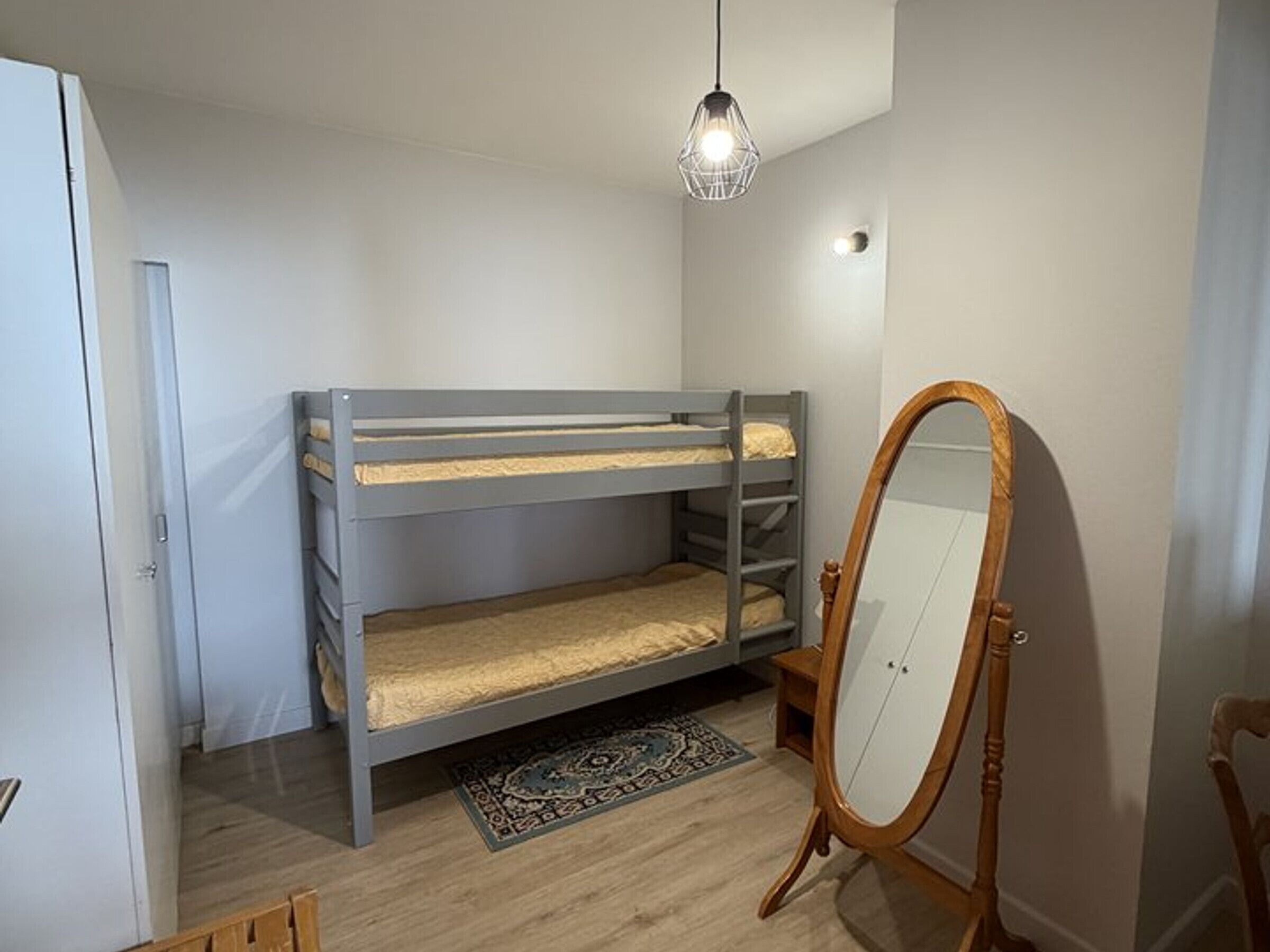 A room with a bunk bed, a wooden-framed mirror, and a hanging light fixture.