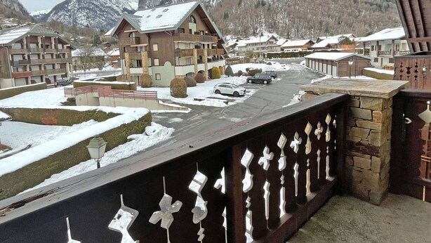 Eine verschneite Bergstadt mit Chalets, einem Parkplatz und einem Balkon mit schmiedeeisernen Geländern.