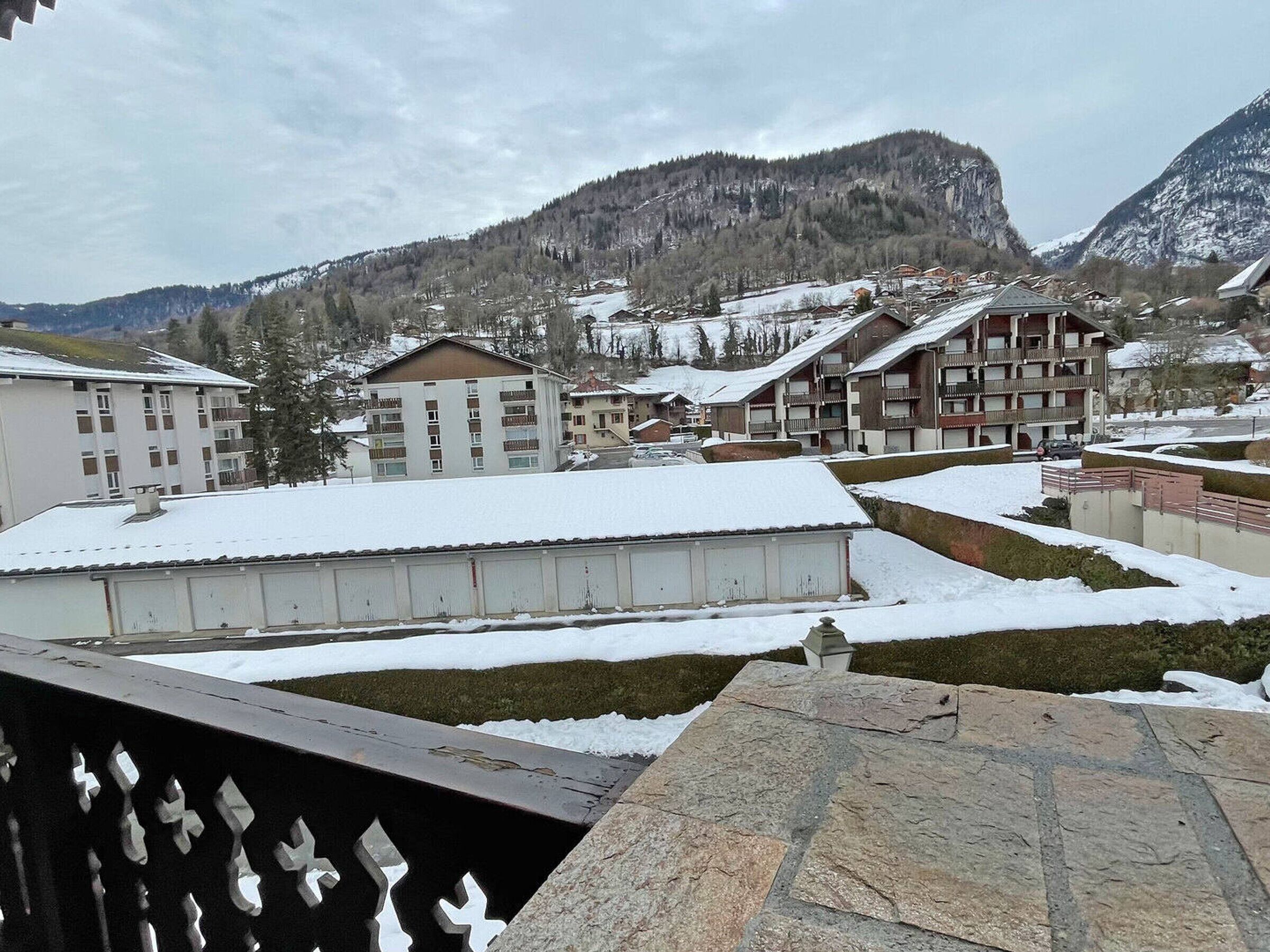 Un quartier résidentiel enneigé, avec des immeubles à plusieurs étages, une montagne en arrière-plan et une allée pavée au premier plan.