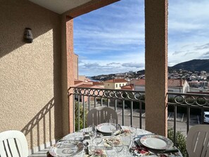 A balcony with a table set for dining, overlooking a cityscape with buildings and a mountain in the distance. - 2-Room Apartment with Parking in Banyuls-sur-Mer (Banyuls-sur-Mer)