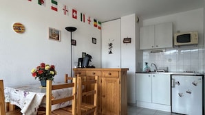 Une cuisine compacte avec des meubles blancs, un petit réfrigérateur et un coin repas comprenant des chaises et une table en bois.