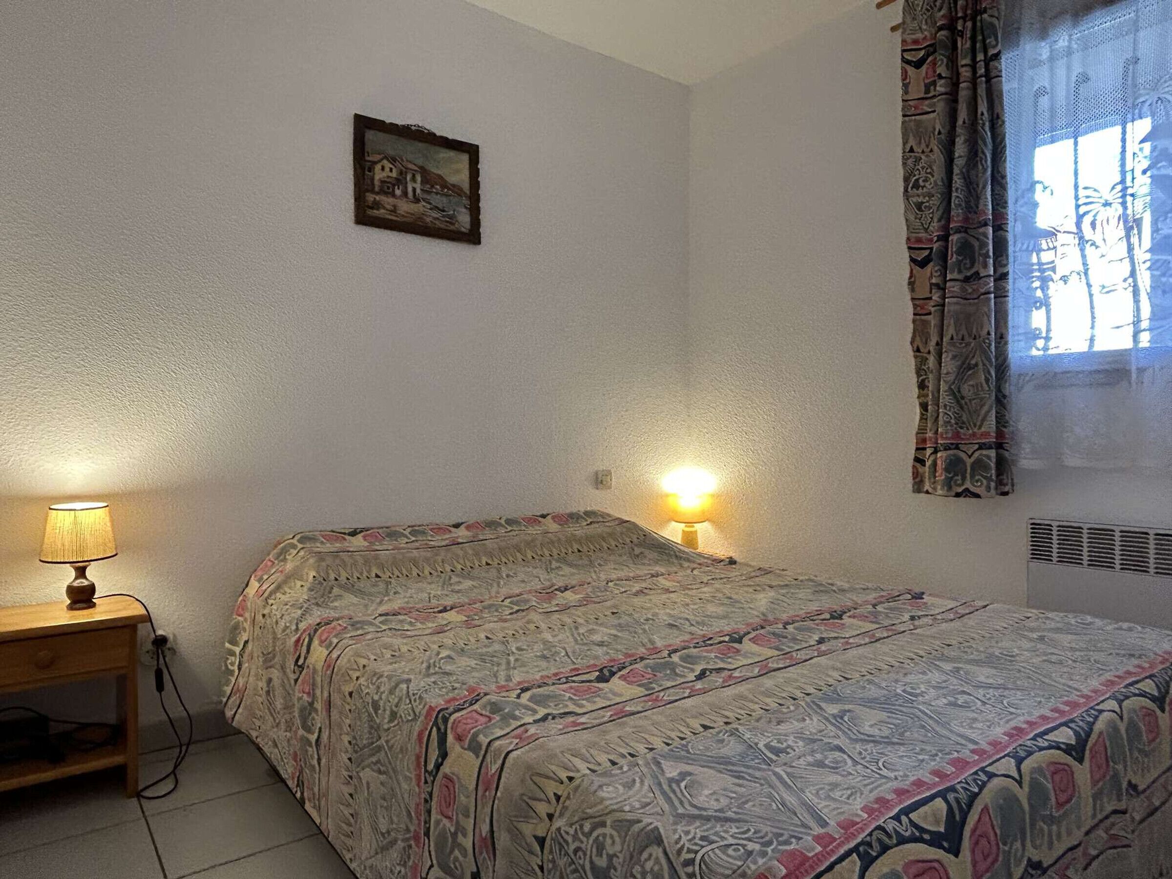 Una camera da letto con un letto, due lampade sui comodini, un quadro appeso al muro e una finestra con tende.
