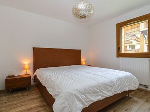 Ein Schlafzimmer mit einem hölzernen Bett, weißer Bettwäsche, zwei Nachttischlampen, einem Nachttisch aus Holz und einem Fenster mit Blick auf Gebäude.