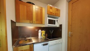 A compact kitchen with wooden cabinets, a microwave, a sink, and a dishwasher. - Cozy Studio on the Slopes - Sleeps 4 (Valmorel)