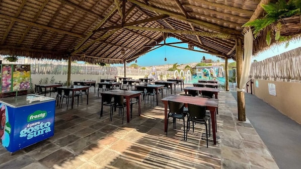An outdoor restaurant with thatched roof, stone flooring, and tables and chairs arranged for dining. - Vila Bertini Icaraizinho (Icaraí de Amontada)