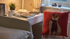 A neatly arranged bedroom with a bed, a desk with a lamp, a window with curtains, and a red pillow with a dog image. - Room-walkinstown Retreat House (Dublin)