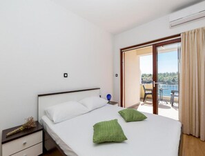 Ein Schlafzimmer mit Bett, Nachttisch, einem kleinen Tisch mit Lampe und Blick auf einen Balkon mit Tisch und Stühlen.