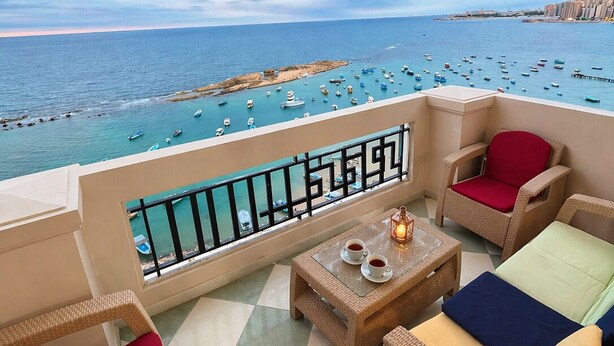 A balcony with wicker furniture, a table with cups, and a view of the sea with boats. - seaview hotel (Alexandria)