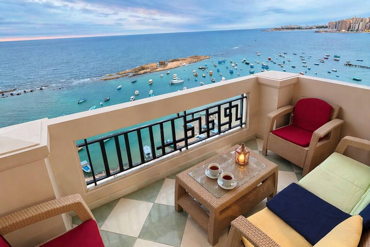 A balcony with wicker furniture, a table with cups, and a view of the sea with boats.