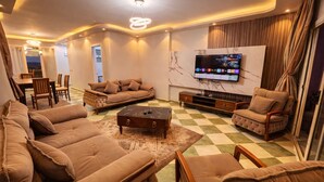 A living room with a sofa set, a coffee table, a TV mounted on the wall, and a dining area with chairs and a table. - seaview hotel (Alexandria)