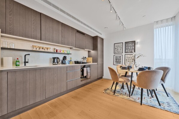 A modern kitchen with wooden cabinets, a built-in oven, and a dining area with a table and chairs. - Comfortable & Peaceful 2BR Apartment Near King’s Cross (London)