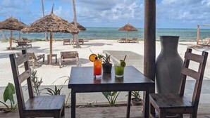 Un restaurant situé en bord de mer, doté de parasols en chaume, de tables et de chaises en bois, et offrant une vue sur l’océan.