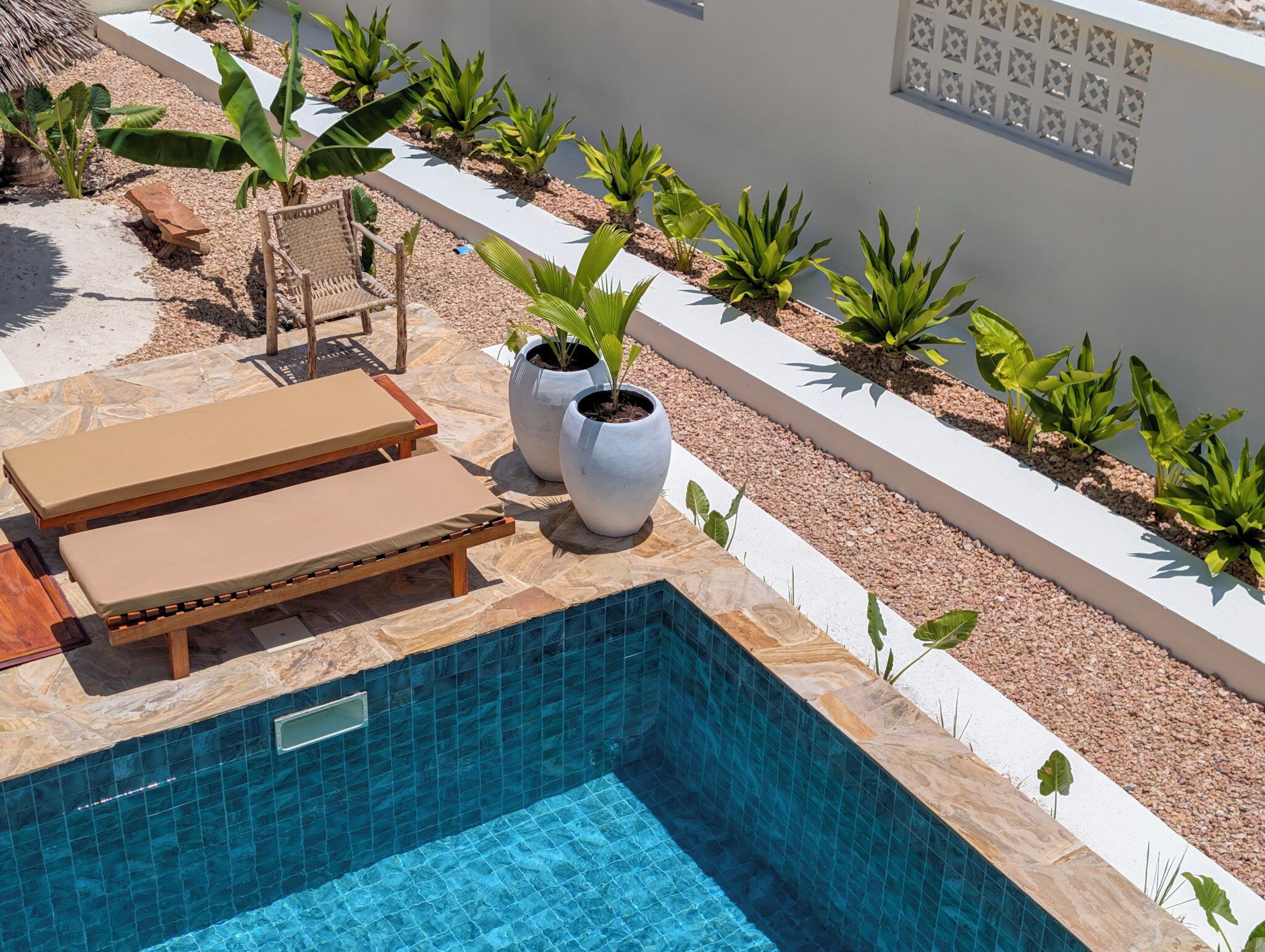 A swimming pool with lounge chairs, potted plants, and a decorative wall.