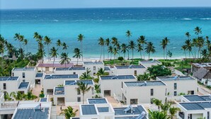 Un hôtel situé sur la côte, composé de plusieurs bâtiments, avec une plage et des palmiers.