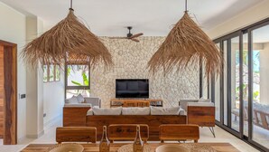 Un salon moderne avec un mur en pierre, un téléviseur à écran plat et un coin repas doté de meubles en bois et de sets de table en fibres tressées.