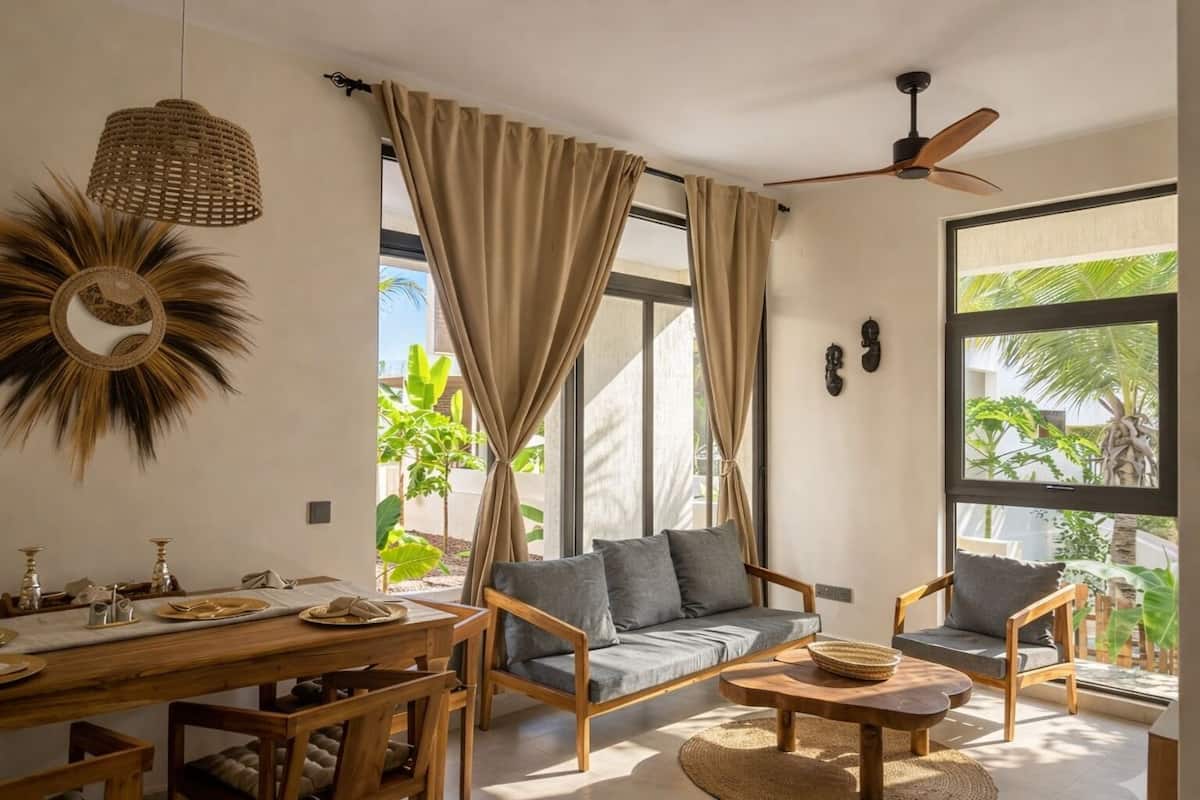 Ein modernes Wohnzimmer mit einer Couch, Sesseln, einem Esstisch und einem Deckenventilator.