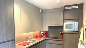 Una cocina moderna con armarios grises, un lavamanos de acero inoxidable, un tostador rojo y un microondas integrado.